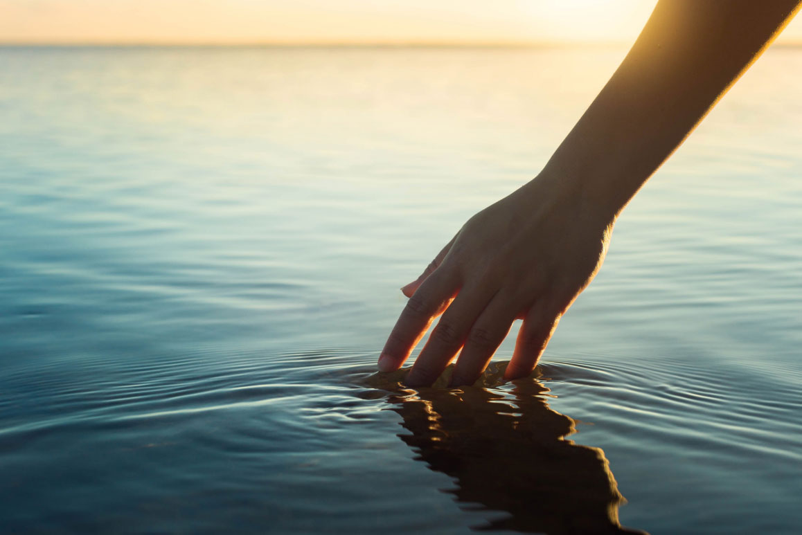 person's hand in clear water at sunset