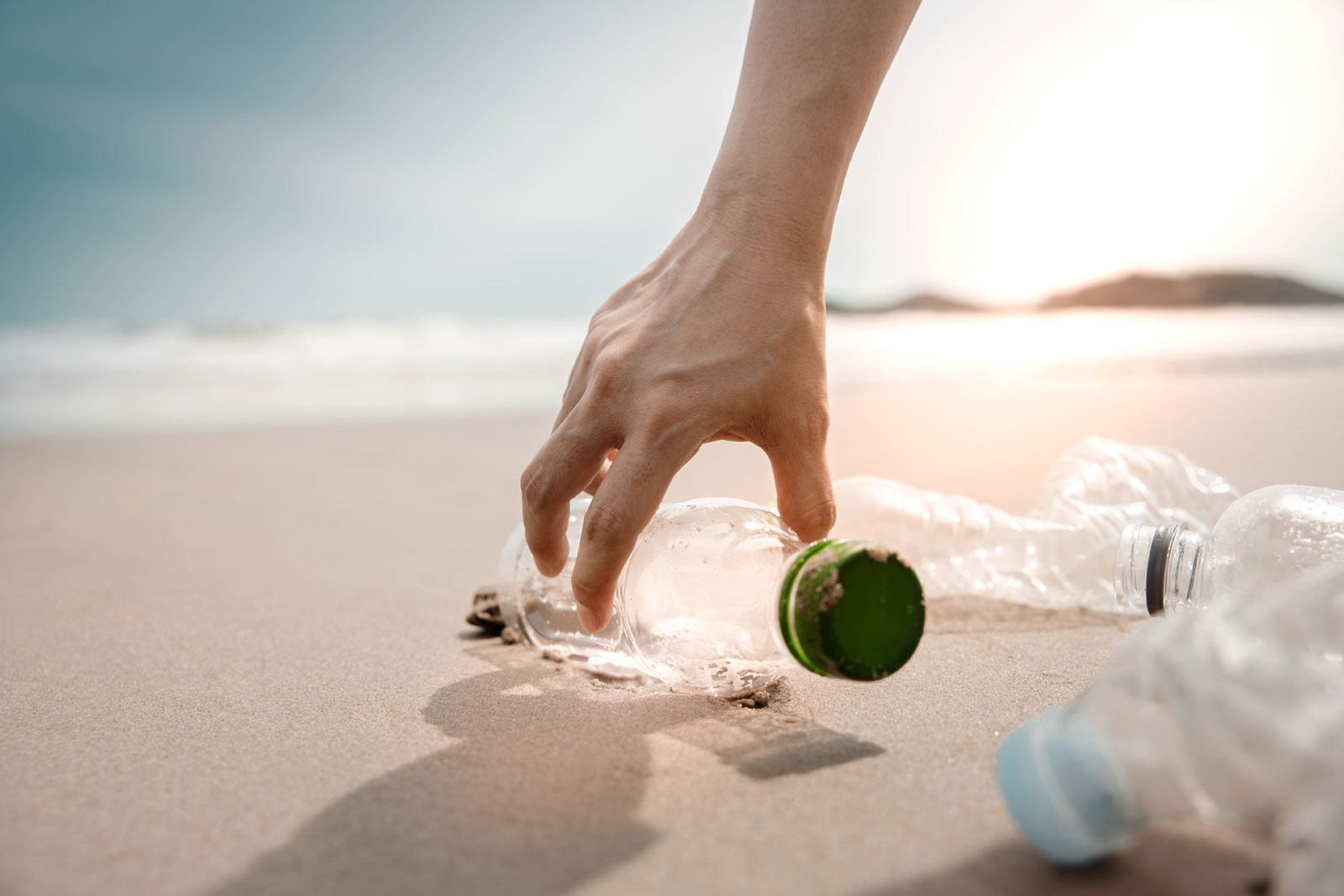 person picking up a plastic bottle from the sea shore - Socially Responsible Investing